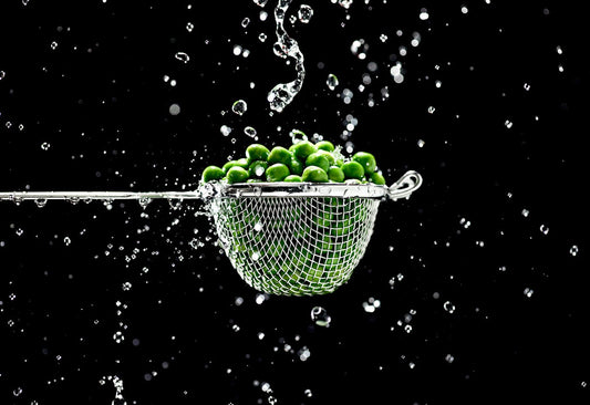 green peas in a strainer amidst a splash of water, representing how pea protein stacks up against whey protein