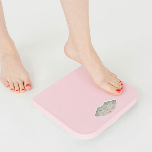 woman's dainty feet being placed on a pink colored weighing scale representing the question around whether protein causes weight gain